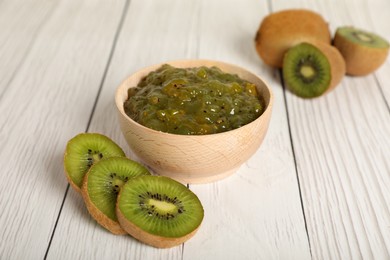 Photo of Bowl of delicious kiwi jam and fresh fruits on white wooden table