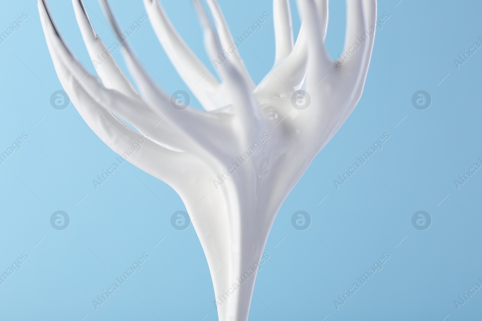 Photo of Whisk with whipped cream on light blue background, closeup