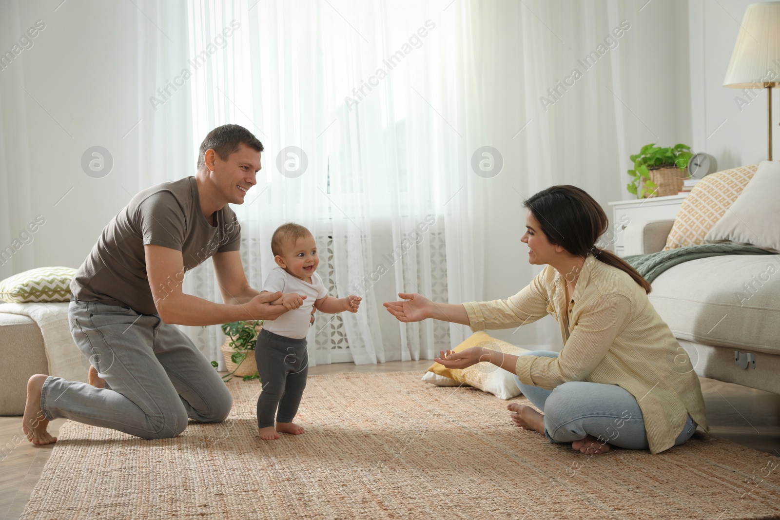 Photo of Parents supporting their baby daughter while she learning to walk at home