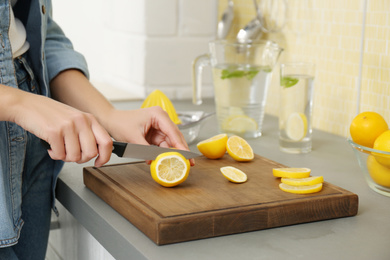 Young woman cutting lemon for refreshing drink in kitchen, closeup