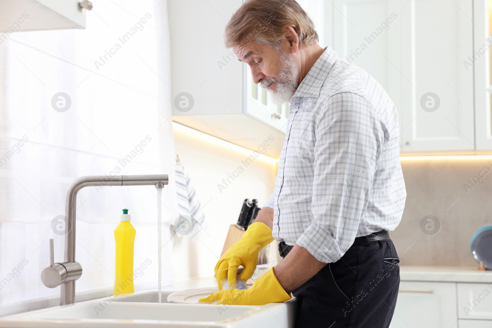 Photo of Senior man in protective gloves washing plate above sink in kitchen