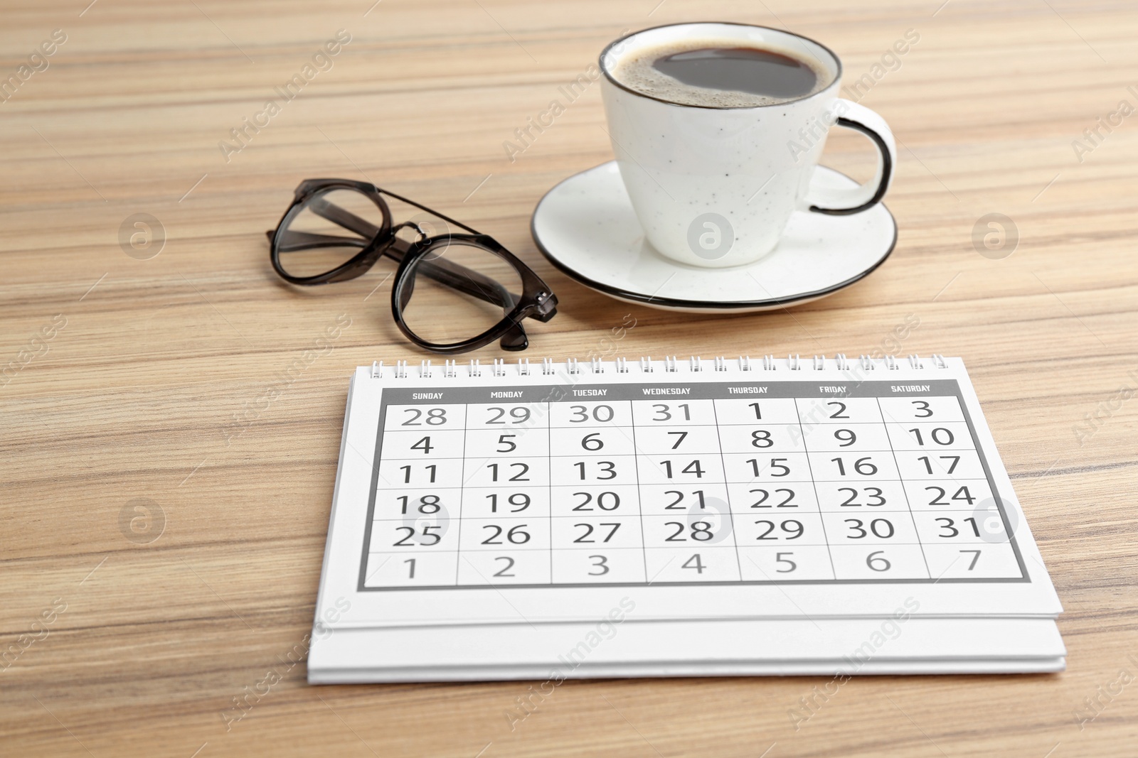 Photo of Paper calendar, cup of coffee and glasses on wooden table