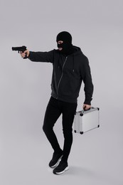 Man wearing black balaclava with metal briefcase and gun on light grey background