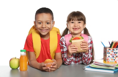 Photo of Schoolchildren with healthy food and backpacks sitting at table on white background