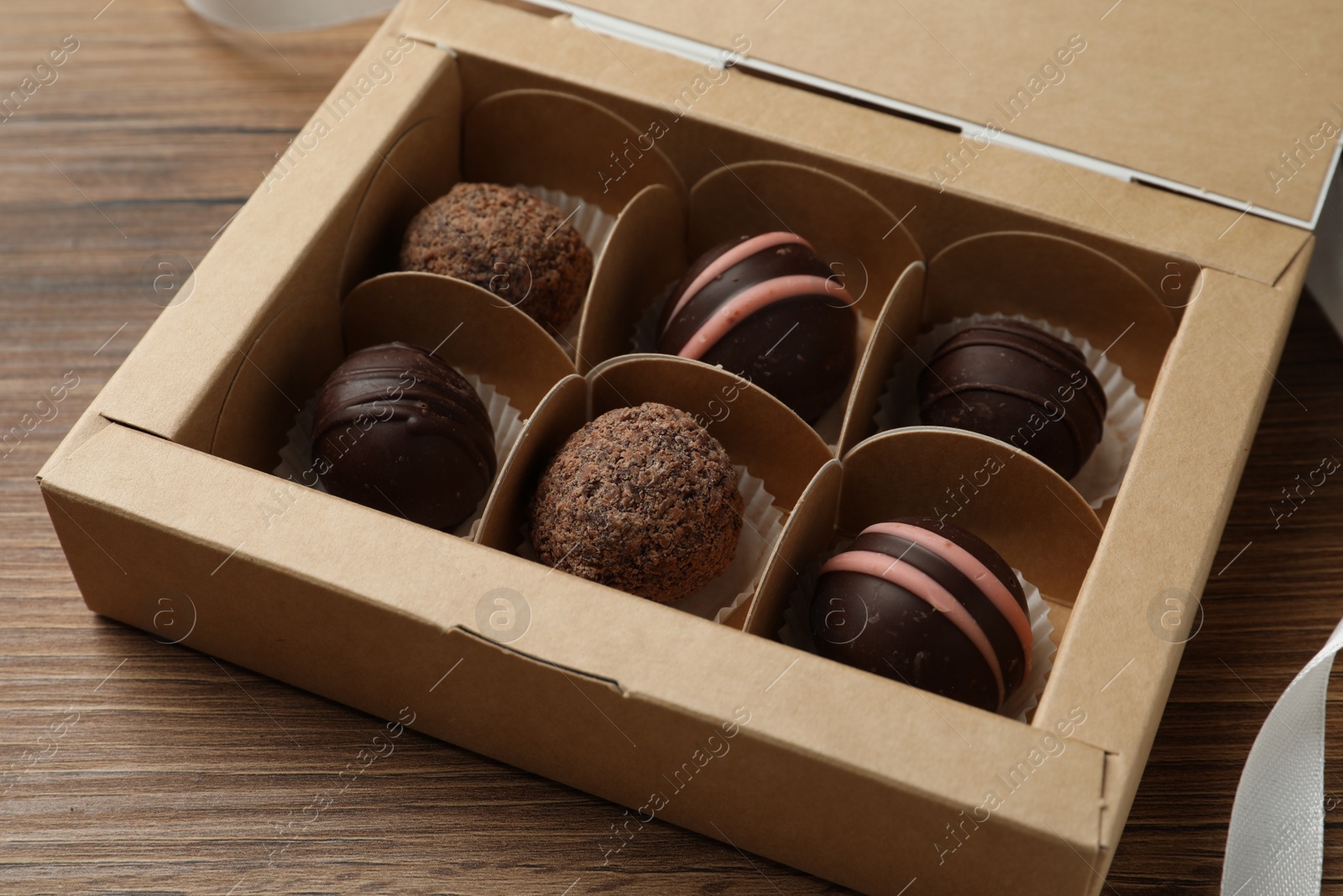 Photo of Many different delicious chocolate truffles in box on wooden table, closeup