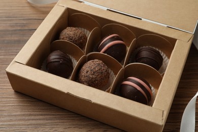 Photo of Many different delicious chocolate truffles in box on wooden table, closeup