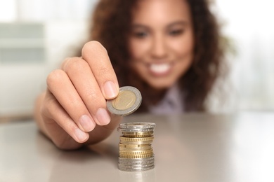 Photo of Young African-American woman stacking coins at table, focus on hand