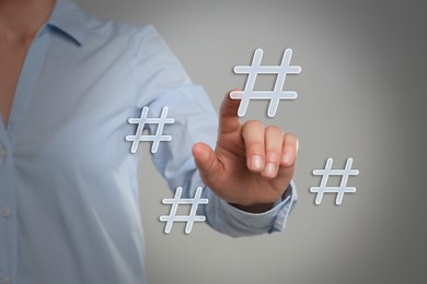 Image of Hashtag concept. Woman pointing at sign on light grey background, closeup