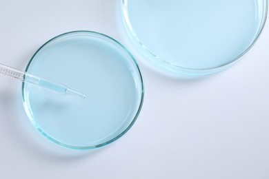 Photo of Dripping liquid from pipette into petri dish at white background, top view. Laboratory analysis