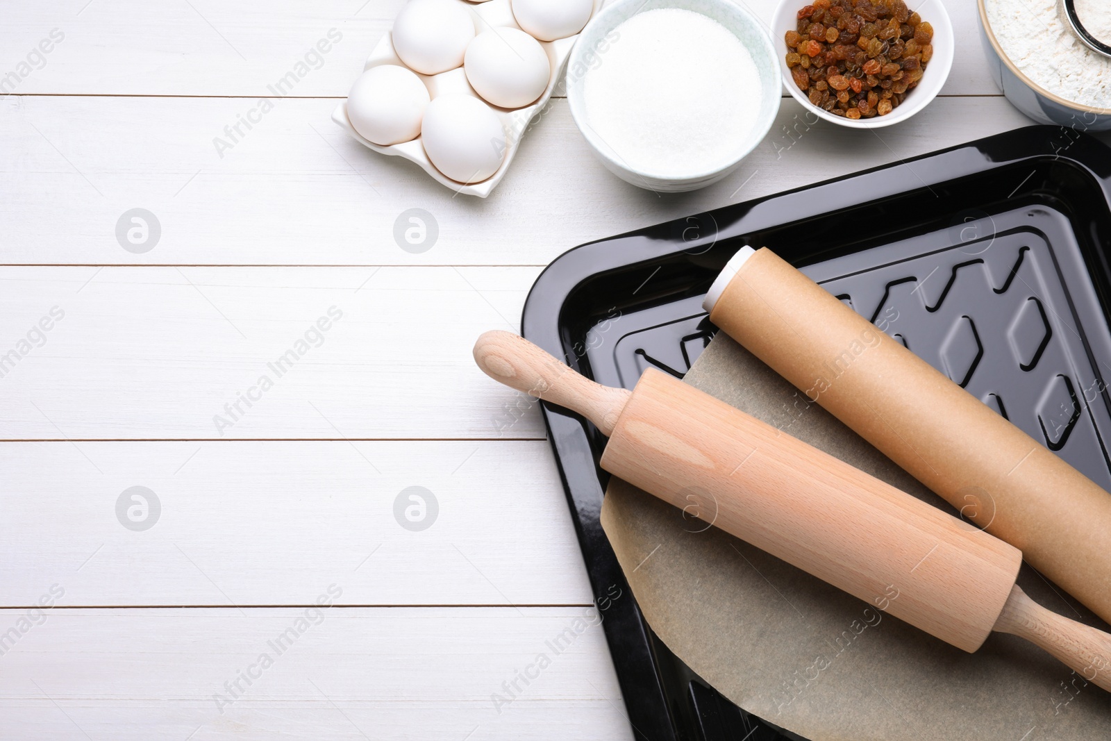 Photo of Baking pan with parchment paper, different ingredients and kitchen tools on white wooden table, flat lay. Space for text