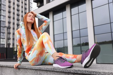 Photo of Beautiful woman in gym clothes sitting on parapet on street