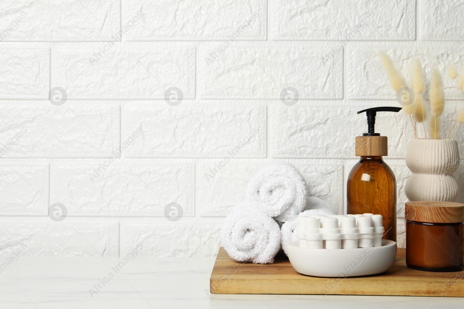 Photo of Different bath accessories, personal care products and spikelets in vase on white table near brick wall, space for text
