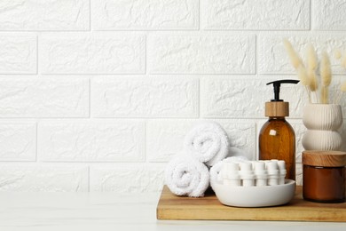 Different bath accessories, personal care products and spikelets in vase on white table near brick wall, space for text