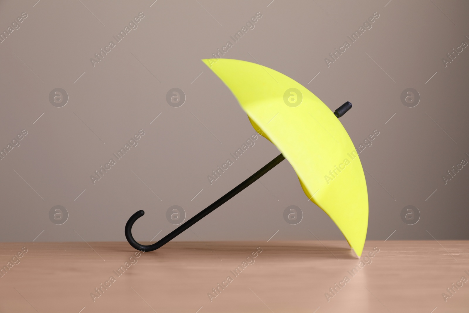 Photo of Small yellow umbrella on wooden table against beige background