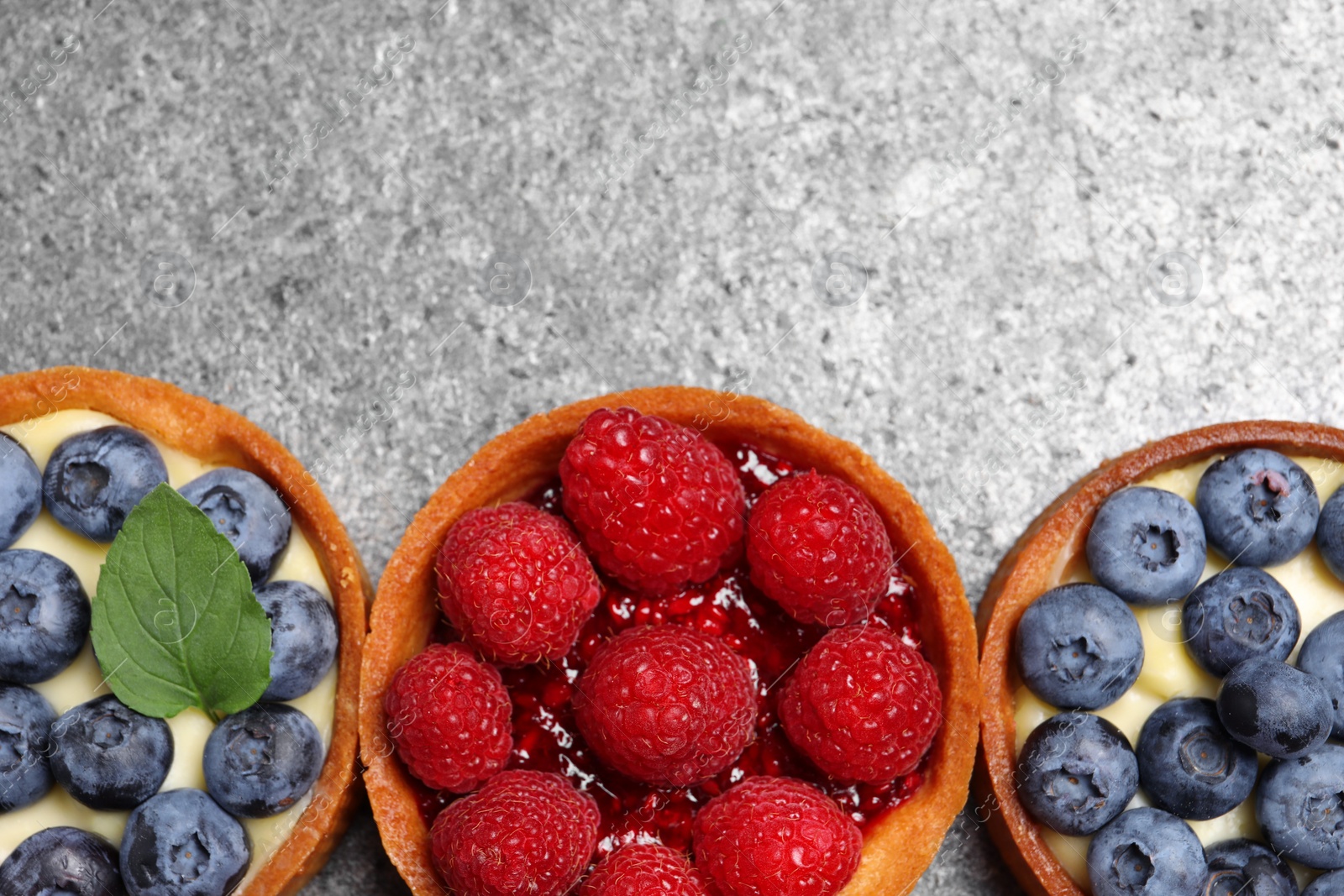 Photo of Tartlets with different fresh berries on light grey table, flat lay and space for text. Delicious dessert