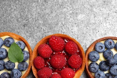 Photo of Tartlets with different fresh berries on light grey table, flat lay and space for text. Delicious dessert