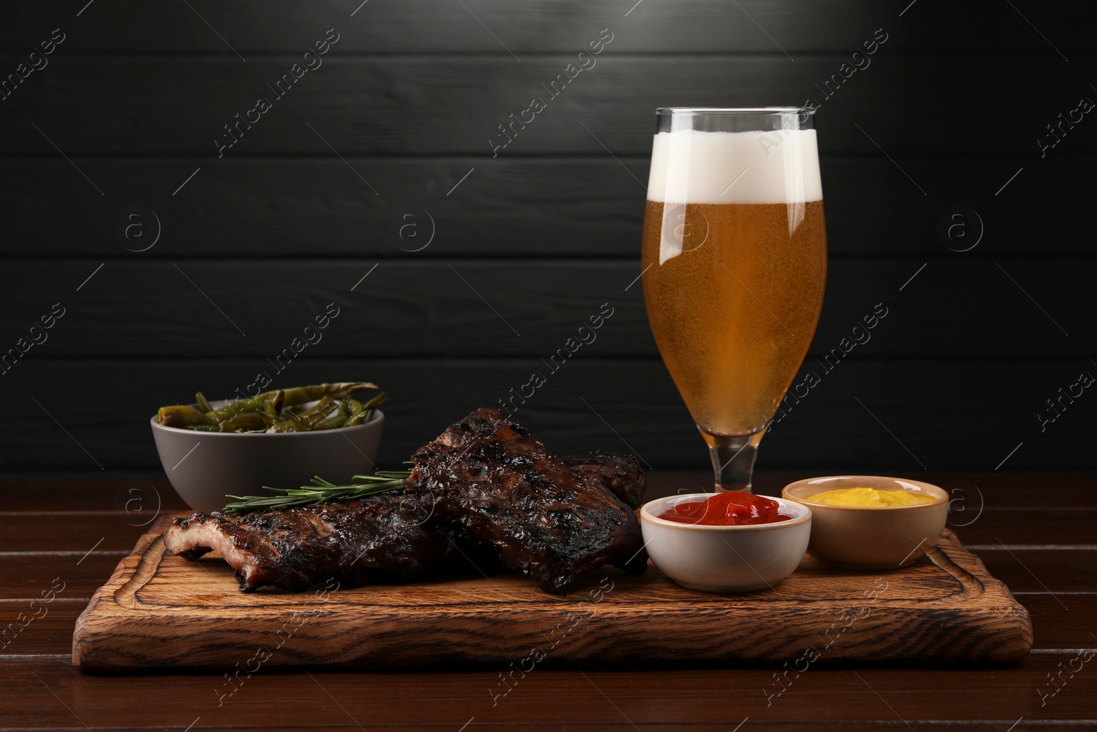 Photo of Glass of beer, delicious grilled ribs and sauces on wooden table