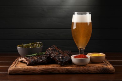 Glass of beer, delicious grilled ribs and sauces on wooden table