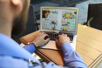 Photo of Man reading online magazine on laptop at wooden table, closeup