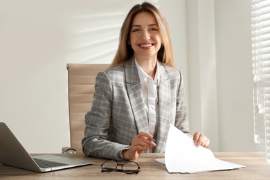 Portrait of beautiful young businesswoman with laptop at table in office