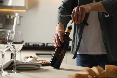 Photo of Man opening wine bottle with corkscrew at table indoors, closeup