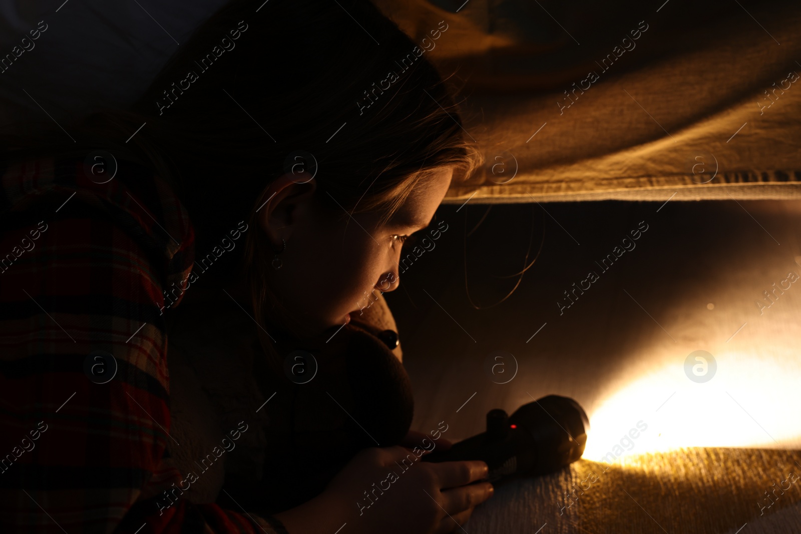 Photo of Little girl with flashlight looking for monster under bed at night