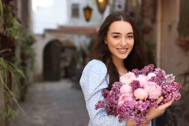 Beautiful woman with bouquet of spring flowers outdoors, space for text