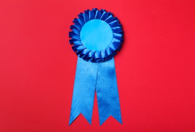 Photo of Blue award ribbon on red background, top view