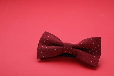 Stylish burgundy bow tie on red background, space for text