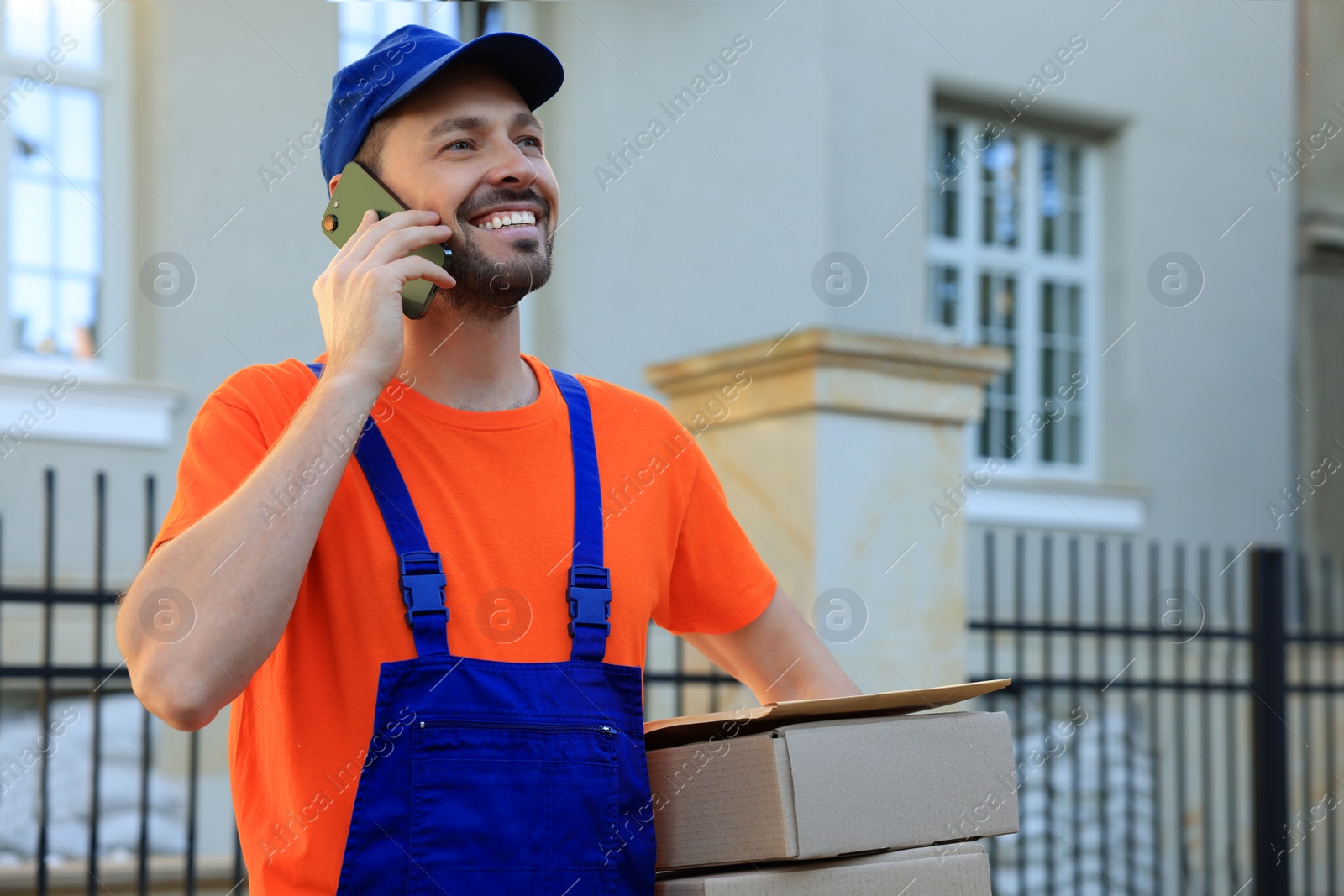 Photo of Courier with parcels talking on smartphone outdoors, space for text. Order delivery