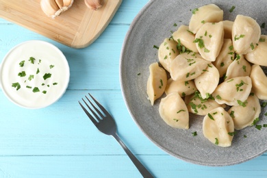 Delicious cooked dumplings with sour cream on light blue wooden table, flat lay