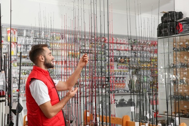 Salesman with fishing rods in sports shop. Space for text