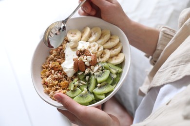 Woman eating tasty granola indoors, closeup view