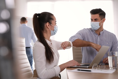 Photo of Coworkers with protective masks making elbow bump in office. Informal greeting during COVID-19 pandemic