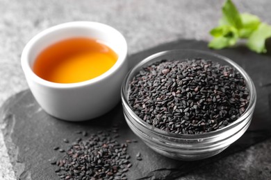 Black sesame seeds and oil on grey table, closeup