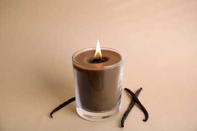 Beautiful candle with wooden wick and vanilla sticks on beige background