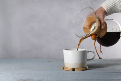 Woman pouring tasty drip coffee into cup at grey wooden table, closeup. Space for text