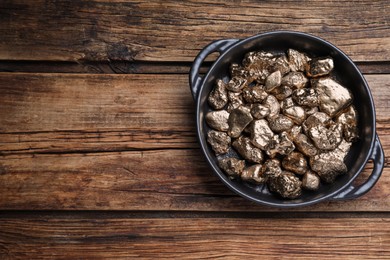 Photo of Pan of gold nuggets on wooden table, top view. Space for text