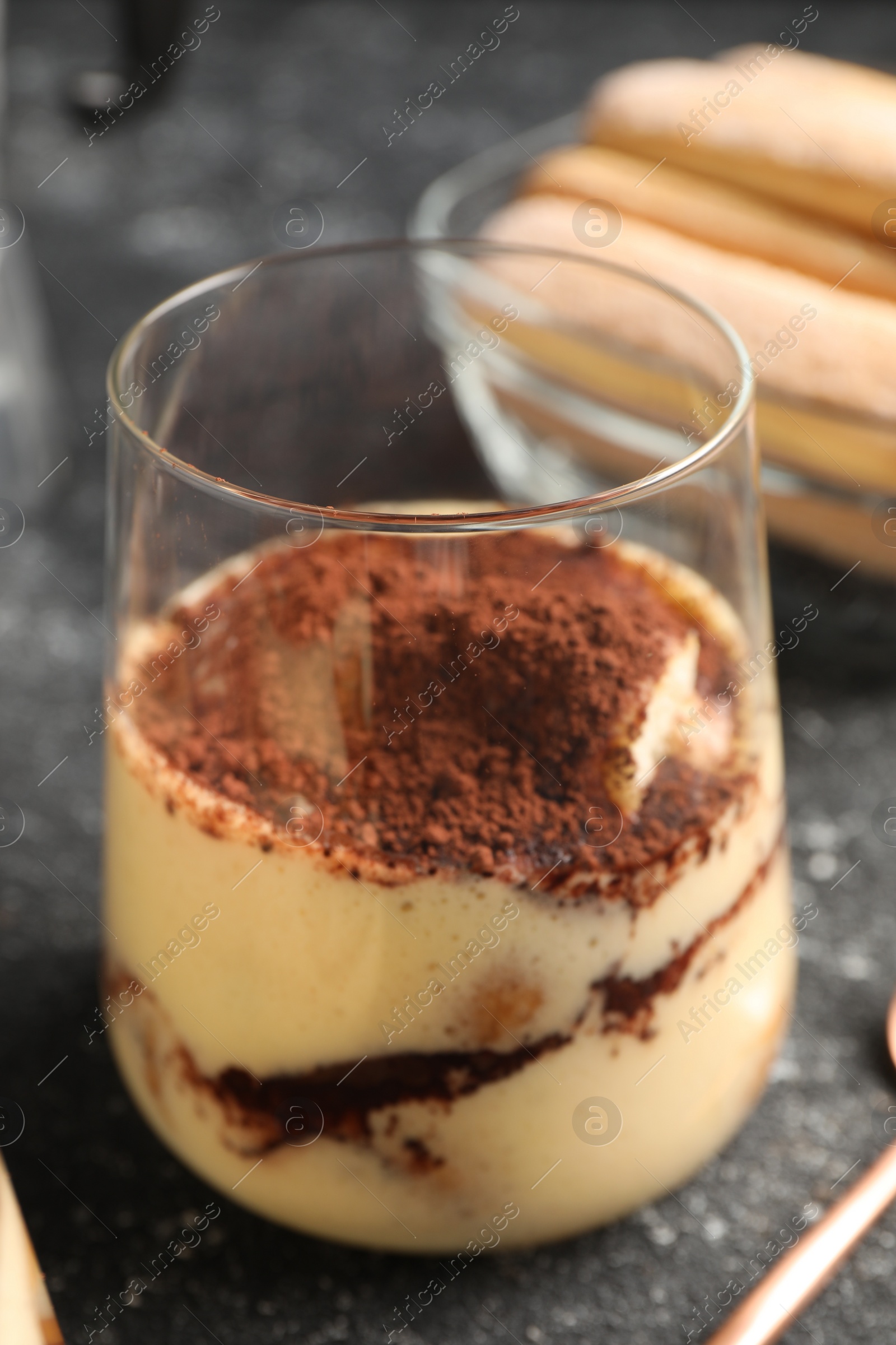 Photo of Delicious tiramisu in glass on grey table, closeup