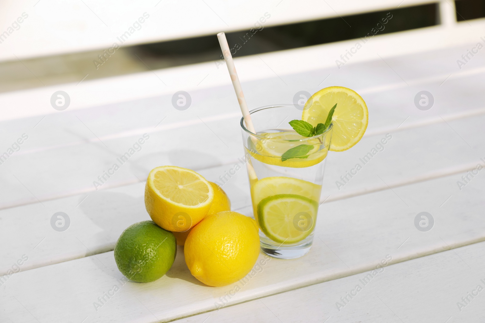 Photo of Glass of water with lemons, limes and mint on white wooden table outdoors