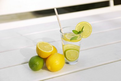 Glass of water with lemons, limes and mint on white wooden table outdoors