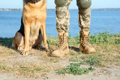 Man in military uniform with German shepherd dog near river, closeup view