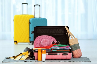 Photo of Modern suitcase full of clothes and accessories on floor indoors