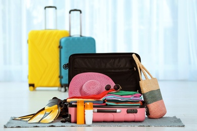 Modern suitcase full of clothes and accessories on floor indoors