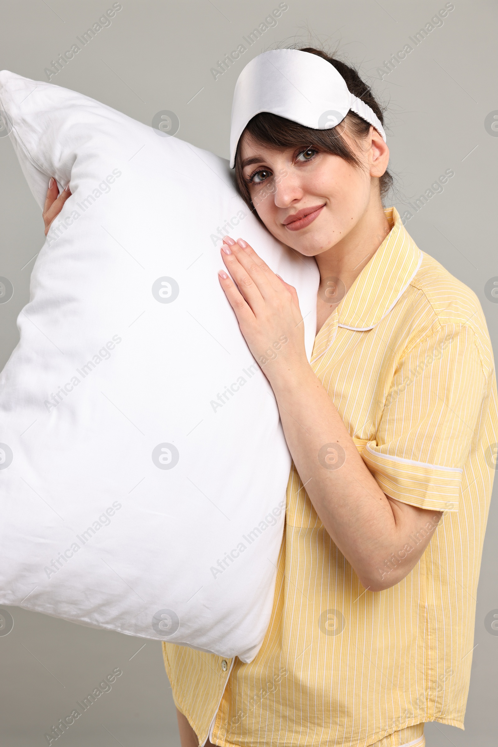 Photo of Woman in pyjama and sleep mask holding pillow on grey background