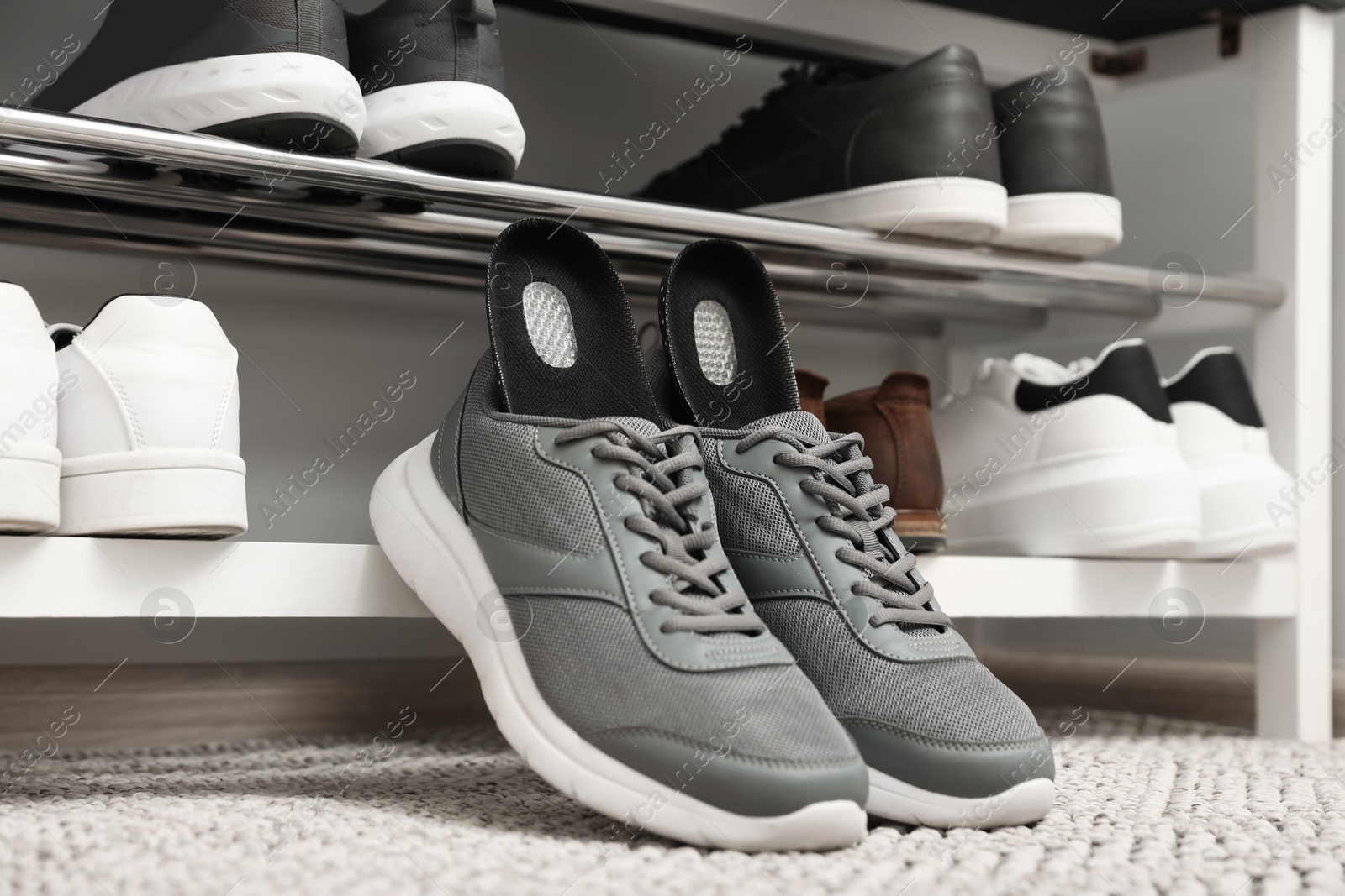 Photo of Orthopedic insoles in shoes on rug near rack, closeup