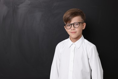 Cute schoolboy in glasses near chalkboard, space for text