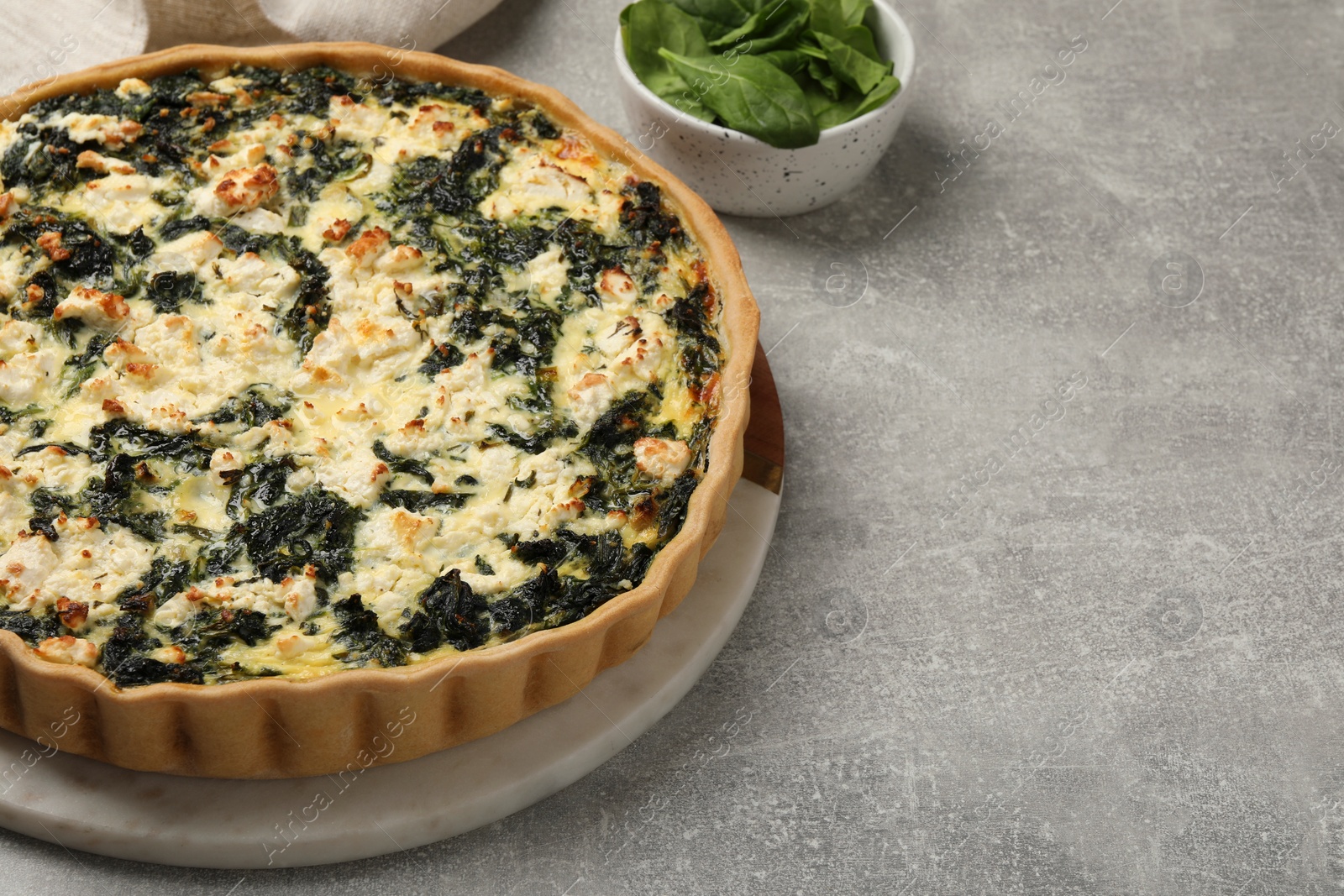 Photo of Delicious homemade spinach quiche on light gray table, closeup. Space for text