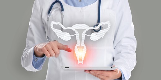 Image of Doctor holding modern tablet and virtual image of uterus on grey background, closeup