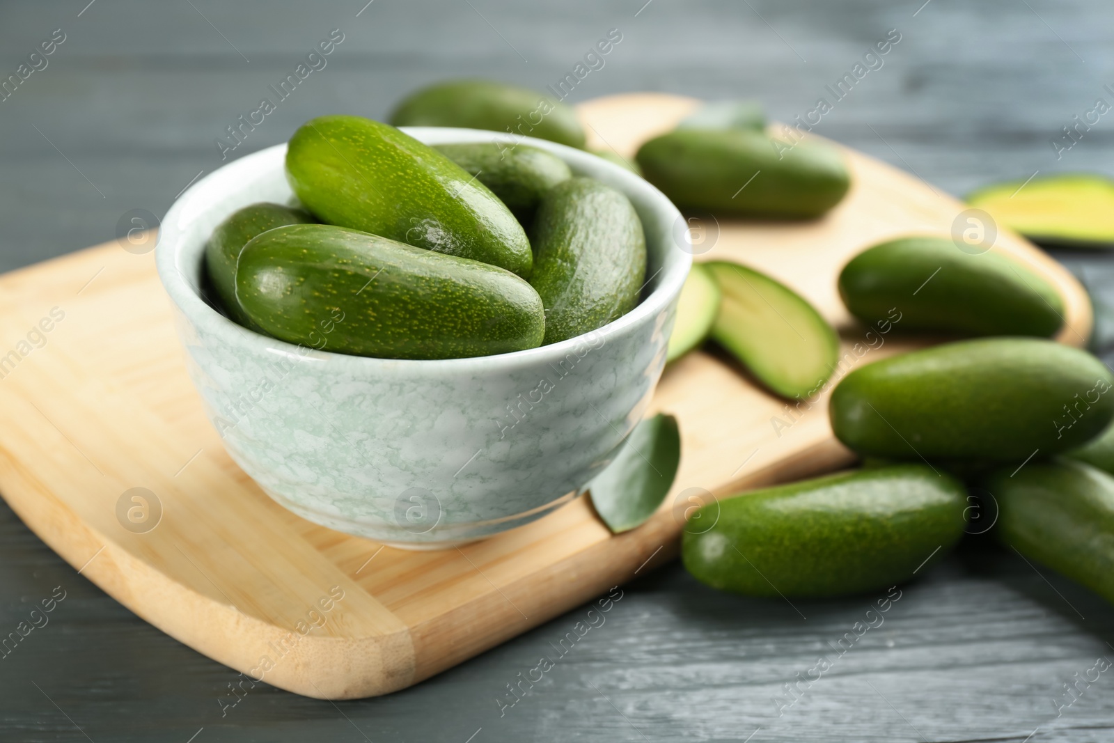 Photo of Fresh seedless avocados in bowl on grey wooden table, closeup